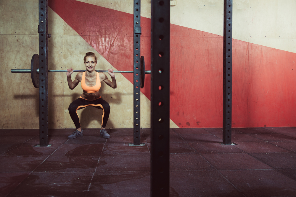 en kvinna som gör knäböj med en skivstång på ryggen inne på ett gym