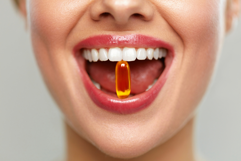en närbild på en glad kvinna som har en omega 3-kapsel i munnen som hon håller mellan tänderna med ett leedende