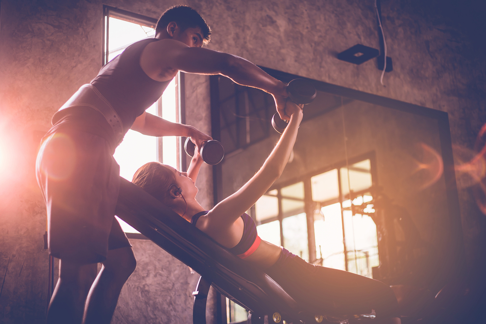 en personlig tränare som hjälper en kvinnlig klient göra bänkpress med hantlar inne på ett gym