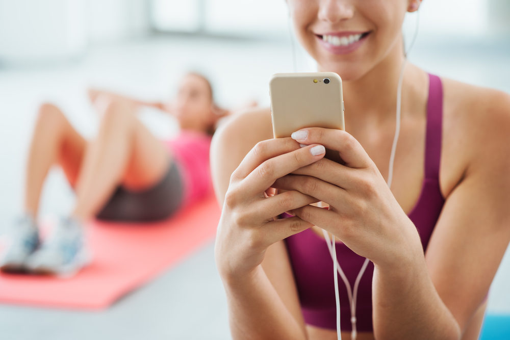 en tjej som ler och tittar på PT Online i telefonen för att hon ska forma kroppen på gymmet