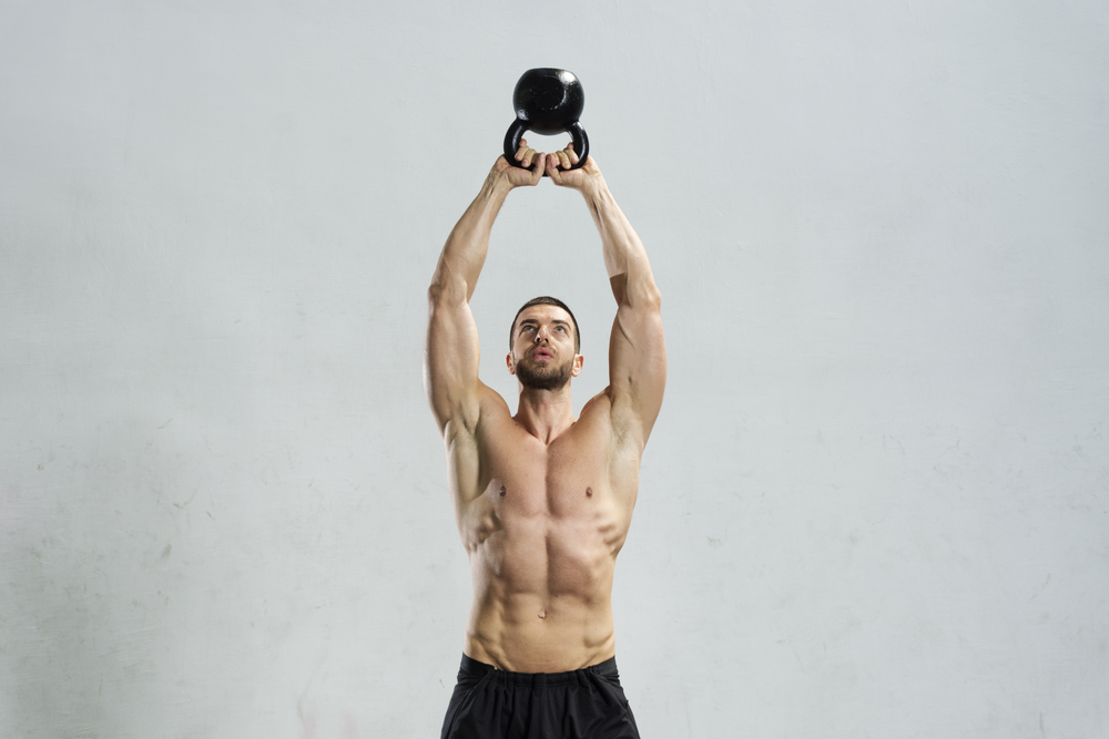 en man utan tröja som svingar en kettlebell ovanför sitt huvud för att han vill bygga muskler