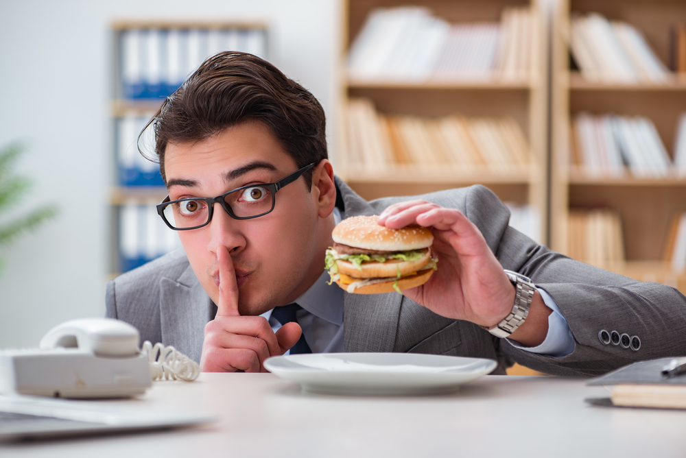 en man med glasögon ska äta en hamburgare för att gå ner i vikt med en extrem diet på sitt kontor