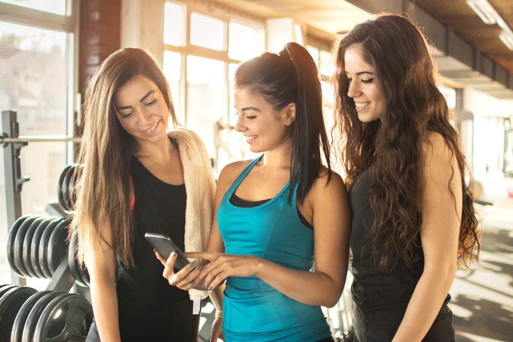 en grupp vänner som är på gymmet och tittar på sin app i mobilen som de får när de har sin gratis pt online