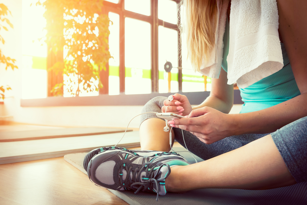 en tjej som har sin pt online i mobilen och sitter på gymgolvet efter ett hårt träningspass ur sitt träningsschema