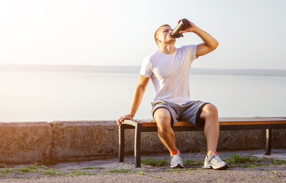 en kille som dricker protein direkt efter gympasset i solen