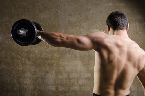 en kille som gör sidolyft med hantel som axelträning för att bygga muskler och stora axlar utan tröja på ett gym