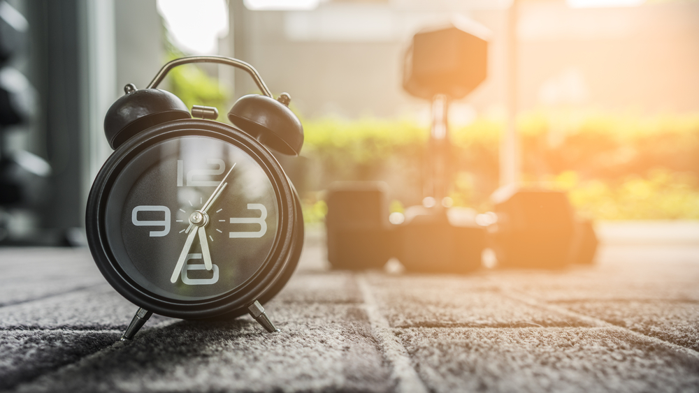 en bild på en klocka och ett hantelpar på ett gym som symboliserar att man kan träna på morgonen med lchf för att gå ner i vikt och bränna fett