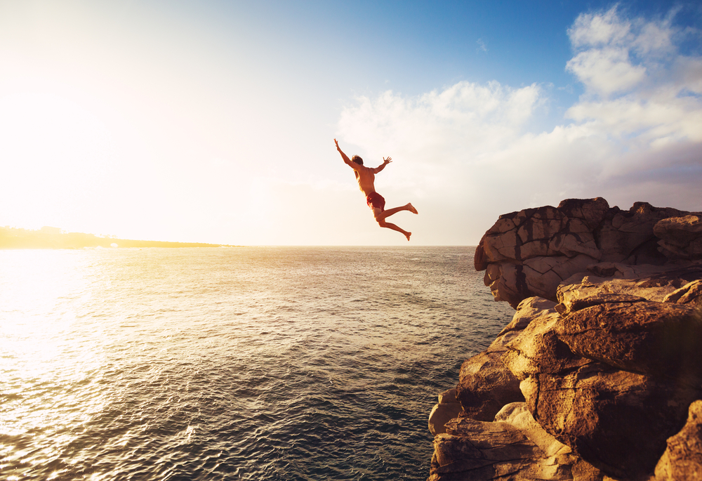 en man som hoppar från en klippa ner i vattnet för att han har stark motivation och inspiration till det