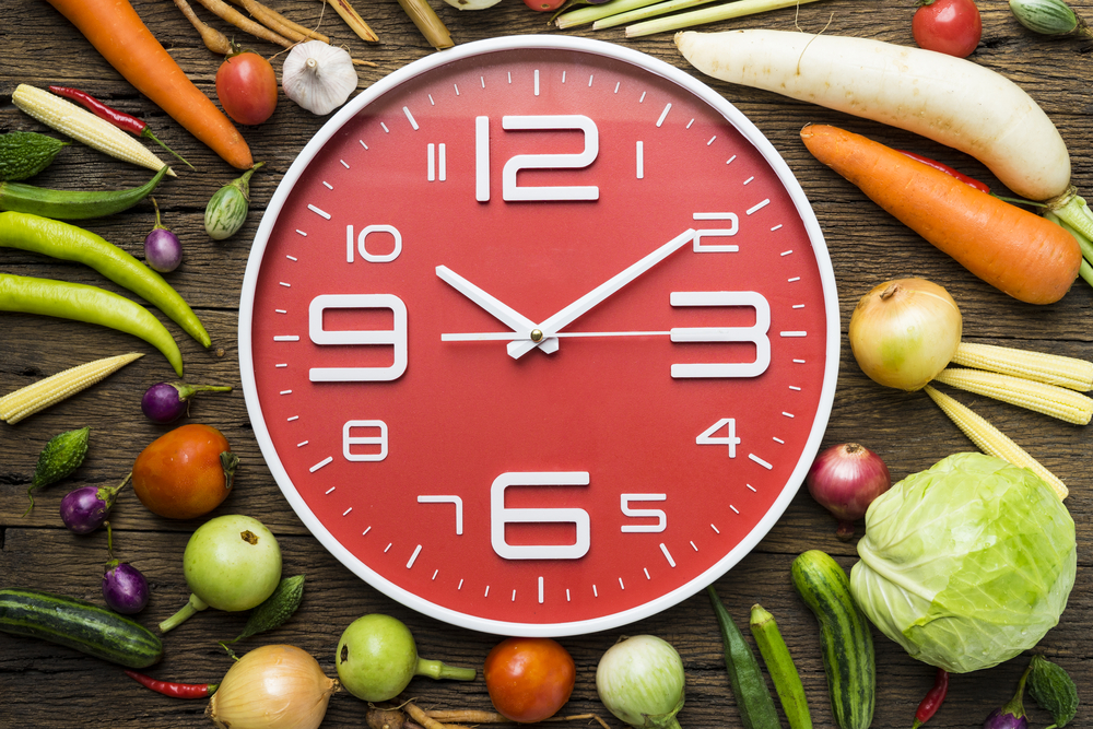 en bild på en klocka bland mat för att symbolisera hur ofta man ska äta för att gå ner i vikt